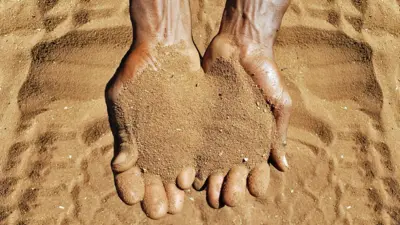 Close-up overhead view of the wrist and hands of an adult male cupping the golden sandy soil of Limpopo Province, South Africa.