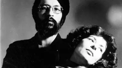A imagem em preto e branco mostra duas pessoas abraçadas. Em primeiro plano, uma mulher (Alice Ruiz) de cabelos ondulados inclina a cabeça para trás e olha para cima, enquanto um homem (Paulo Leminski) com barba, óculos e gorro aparece atrás dela, olhando para frente. O fundo é escuro e desfocado.