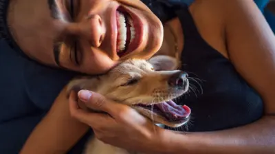 Uma mulher sorri enquanto abraça um cachorro pequeno, com a língua para fora.