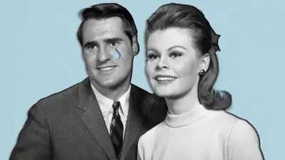 Ifoto y'umweru n'umukara igaragaza umugabo wambaye ikositimu y'umukara, karuvati y'umukara n'ikijuju n'ishati y'umweru, ku jisho rye hariho igitonyanga cy'ubururu kimeze nk'amarira. Yegeranye n'umugore wambaye umupira w'umweru w'amaboko maremare atagaragara yose, yambaye n'iherena ry'umukara. Bombi barimo kumwenyura, bareba imbere. 