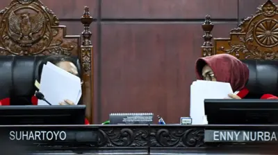Ketua MK Suhartoyo dan Hakim Enny Nurbaningsih sedang berbisik di mana keduanya menutup wajah mereka dengan kertas.