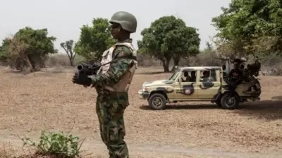 Wani soja tsaye rike da bindiga da motar sojoji a gefensa