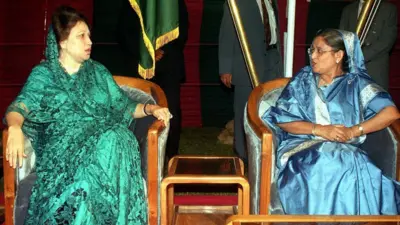 সবুজ শাড়ি পরা খালেদা জিয়া ও নীল শাড়ি পরা শেখ হাসিনা পাশপাশি দুটি চেয়ারে বসে একে অন্যের দিকে তাকিয়ে আছেন