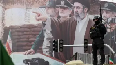 بیلبوردی از مجتبی خامنه‌ای که با دست به جایی اشاره می‌کند اطراف او چند فرمانده سپاه هستند. جلوی بیلبورد یک نیروی نظامی مجهز با چهره‌ای پوشیده دیده می‌شود