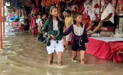 सोमवार को गुरुग्राम में शीतला माता मंदिर के पास भारी बारिश के बाद पैदल चलने वाले लोग पानी से भरी सड़क से गुज़रते हुए