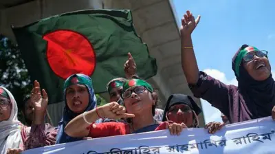 در جریان گردهمایی «جنبش دانشجویی ضد تبعیض» به مناسبت گذشت یک ماه از برکناری شیخ حسینه،  نخست‌وزیر پیشین بنگله‌دیش، در داکا،بنگله‌دیش، در ۵ سپتامبر ۲۰۲۴، جوانی که سربندی با نقش پرچم بنگله‌دیش بر سر دارد، یک پرچم بزرگ بنگله‌دیش را تکان می‌دهد و شعار می‌دهد. پرچم سبز تیره است و در مرکز آن یک دایره قرمز دیده می‌شود. ده‌ها معترض او را احاطه کرده‌اند که بیشترشان سربندهای یکسانی به سر دارند