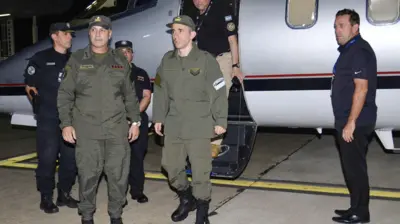 Nahuel Gallo (centro), vestido con su uniforme color verde militar, bajando del avión privado. A su lado ahy 