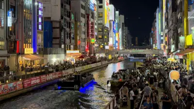 Japonya'nın Osaka kentindeki Dotonbori Kanalı boyunca akşam kalabalıkları. Işıklı reklam panoları, restoranlar ve gezi tekneleri, Namba eğlence bölgesindeki en tanınmış gece hayatı manzaralarından birini oluşturuyor.