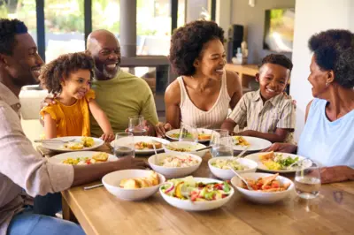 Famille multigénérationnelle assise autour d’une table mangeant un repas à la maison ensemble