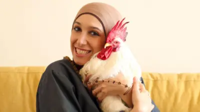 فوزیه روی یک مبل زرد نشسته و خروس سفیدش را در آغوش گرفته است
