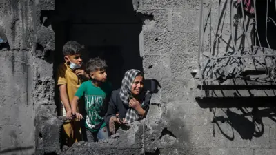 صورة أرشيفية تُظهر طفلين فلسطينييْن وفتاة ينظرون من فتحة وجدت بفعل القصف في منزلهم المدمر عقب غارة جوية إسرائيلية، في مخيم الشاطئ للاجئين، شمال قطاع غزة (29 أكتوبر/تشرين الأول 2025).
