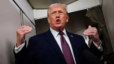 Дональд Трамп в костюме и галстуке стоит в самолете, активно жестикулирует, показывая руками на себя 