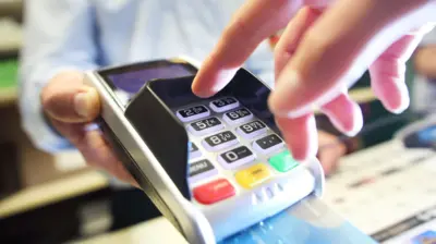 Woman entering pin number into card machine to pay at a shop