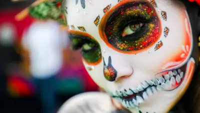 A close up shot of a woman wearing day of the dead make up of a La Catrina, a skull grin in vivid hues of black, white and orange