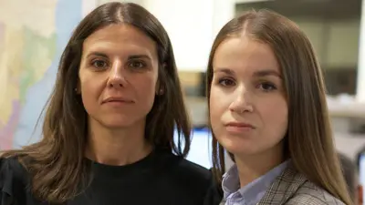 Spanish elite policewomen Cristina and Lidia look at the camera. Cristina is wearing a black top and has long brown hair. Lidia also has long brown hair and is wearing a blue shirt and checked jacket.