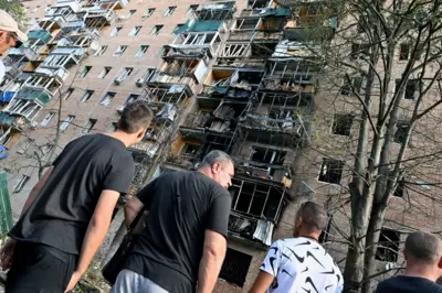 Homens paradosanderson manchester unitedfrente a prédio que foi atingido. Janelas quebradas e fachadas queimadas 