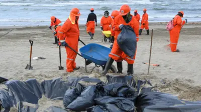 Un equipo de trabajadores limpian las manchas de alquitrán de las playas a lo largo de la orilla del mar en México.