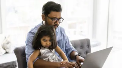 A dad on his laptop with his daughter on his lap