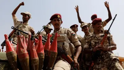 Sete membros do RSF no Sudão, com uniforme militar, boina vermelha com estrela e armas nas mãos
