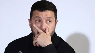 Владимир Зеленский задумчиво смотрит вбок, прикрыв ладонью рот