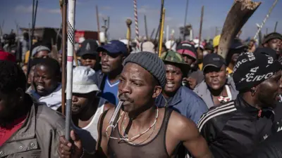Man hold club odas hold stick for im back, during protest for South Africa