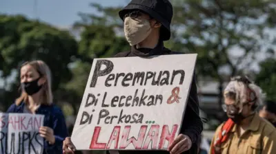 Seorang demonstran yang mengenakan masker memegang plakat menentang kekereasan terhadap perempuan.