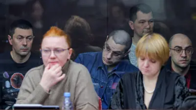 На переднем плане сидят две женщины - адвокаты, на заднем плане обвиняемые мужчины с серьезными сосредоточенными лицами