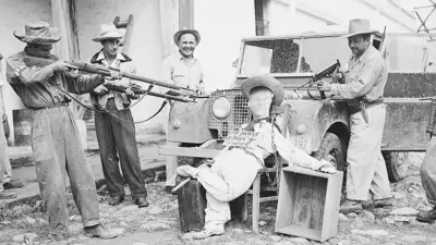 Fotografia em preto e branco de membros do Exército da Libertação apontando armas para uma efígie acorrentada do presidente guatemalteco Jacobo Árbenz, apoiado sobre um veículo militar com um cartaz dizendo 'Estão me chamando da Rússia com [meu predecessor, Juan José] Arévalo'.