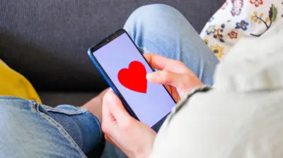 Pessoa sentada olhando para o telefone celular, que mostra um coração na tela.
