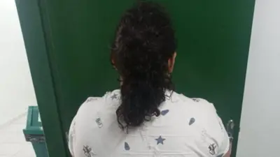 Back view of a woman in a white blouse with dark hair tied up in a pony tail. She is standing in front of a dark green door.