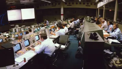 Sala de controle de missão espacial, repleta de pessoas