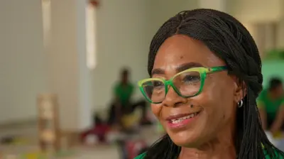 A close-up photo of Nonye Nweke wearing green glasses. She has long hair.