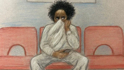 A court sketch of Axel Rudakubana sitting on a red chair. He has black, curly hair and is wearing a grey sweatshirt and joggers. He has his sweatshirt pulled up over his face, only his eyes are visible. 