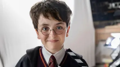 Dominic McLaughlin as a young Harry Potter, wearing spectacles and a school uniform