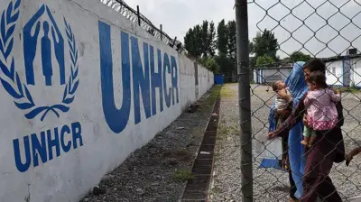 یک خانواده مهاجر افغان در کنار دیواری که روی آن لوگوی کمیساریای عالی پناهندگان نقاشی شده