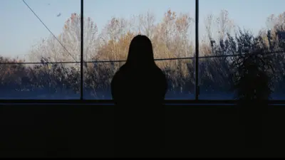 一名女子凝視窗外的剪影，背景為樹木與綠意。