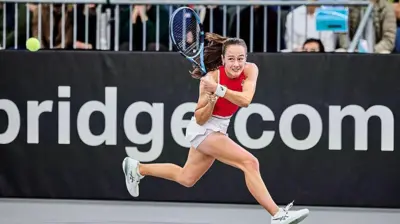 Uzun saçlı bir kadın kırmızı üst ve beyaz şort etekle kortta. Raketle forehand vuruyor.