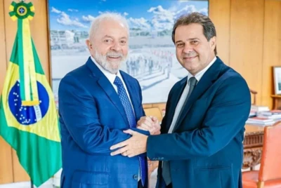 Lula e Evandro Leitão sorrindo para foto, ambos de terno, ao fundo uma bandeira do Brasil