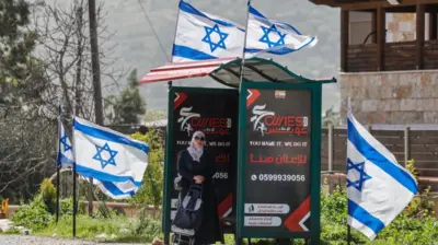 Filistinli bir kadın, İsrail işgali altındaki Batı Şeria'da, Nablus ve Ramallah arasında, Luban-e-Şerkiya yakınlarındaki bir otobüs durağında İsrail bayraklarının yanında bekliyor