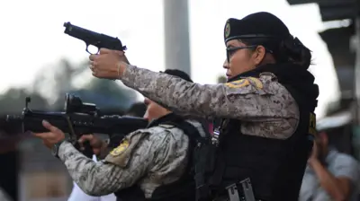 Una funcionaria de policía apunta con su arma. A su lado, otro agente, apunta con un fusil. 