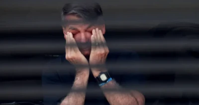 Imagem mostra Bolsonaro atrás das grandes de sua casa. Ele coloca as mãos nos olhos em pose que parece demonstrar cansaço