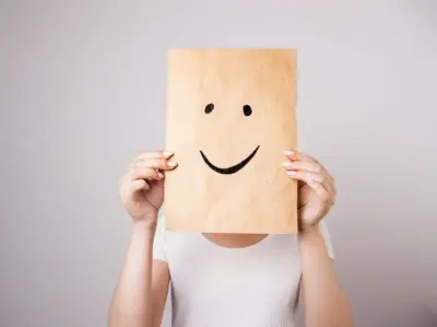 Mulher cobrindo o rosto com papel com um sorriso desenhado