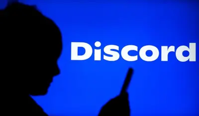 A sombra de uma pessoa de perfil usando o celular, em frente a um fundo azul com o logotipo do Discord