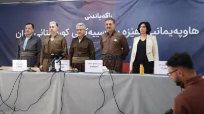 Parti liderleri ayakta duruyor. Önlerinde partilerinin isimleri yazdığı ve mikrofonların bulunduğu bir masa var. Beş liderden dördü erkek, biri kadın.