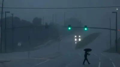 A man with an umbrella crosses a road as Hurricane Milton approaches, in Orlando, Florida