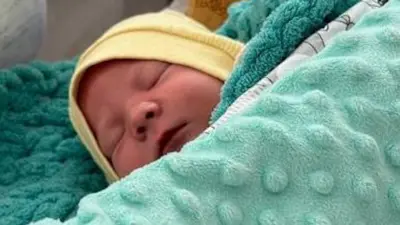 W kijowskim szpitalu na łóżku leży śpiące niemowlę w żółtej czapeczce, przykryte jasnozielonym kocykiem.