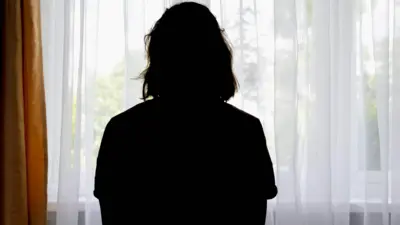 Tül perdesi çekilmiş bir pencereden dışarı bakan bir kadının arkadan görüntüsü 