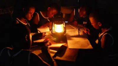 Awọn akẹkọọ marun joko yi tabili kan kan , wọn n ka iwe, atupa kan wa laarin tabili naa, ti gbogbo ayika wọn si sokunkun