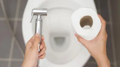 Bir kadın bir elinde taharet musluğu diğerinde tuvalet kağıdı tutuyor
