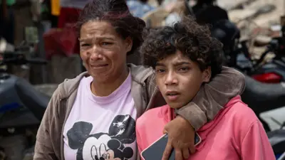 Dos personas compungidas, rodeadas de la destrucción causada por los terremotos de Venezuela. 